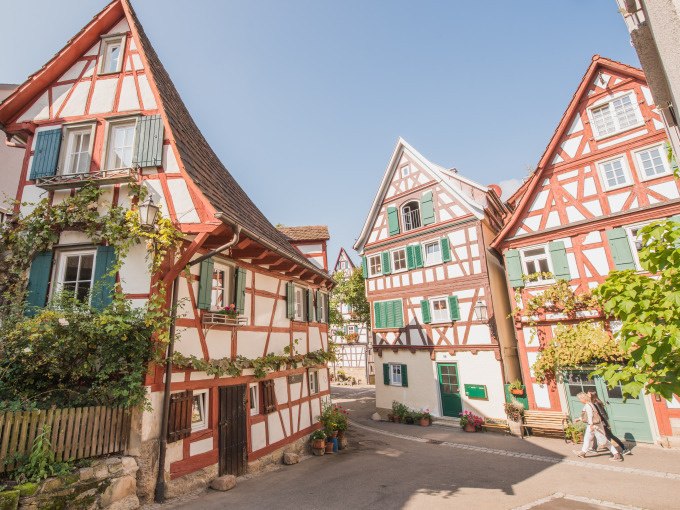 Fachwerkhäuser in Schorndorf mit roten Balken und grünen Fensterläden, umgeben von Pflanzen, unter blauem Himmel., © Eigenbetrieb Tourismus und Citymanagement Schorndorf