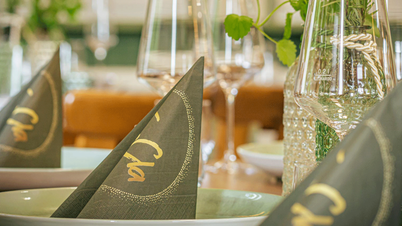 Ein elegant gedeckter Tisch mit gefalteten Servietten, Gläsern und dekorativen Elementen. Die Servietten tragen den Schriftzug 'Cla'., © FreCla Gastronomiebetriebe GmbH