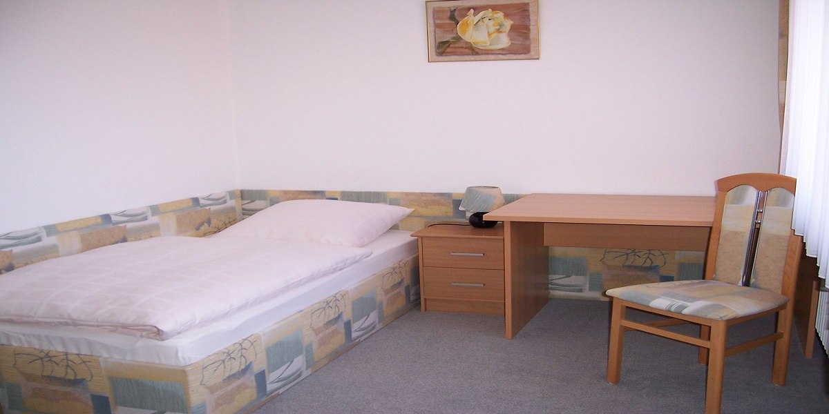 Ein schlichtes Zimmer mit Einzelbett, Schreibtisch, Stuhl und Nachttisch. An der Wand hängt ein Blumenbild., © Hotel Traube