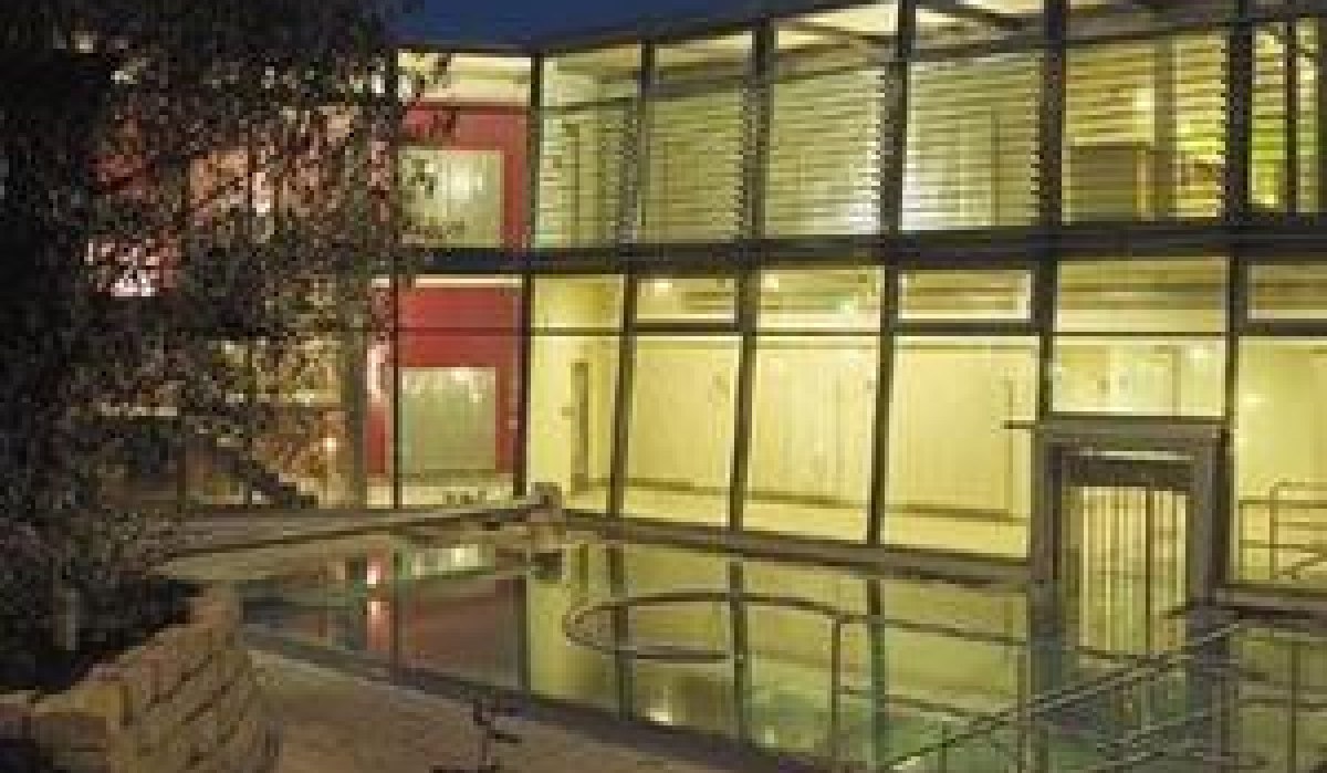 Modernes Gebäude mit Glasfassade, beleuchtet bei Nacht. Ein kleiner Pool oder Wasserfläche spiegelt das Licht wider. Bäume im Vordergrund., © Schwäbische Alb Modernes Gebäude mit Glasfassade, beleuchtet bei Nacht. Ein kleiner Pool oder Wasserfläche spiegelt das Licht wider. Bäume im Vordergrund., © Schwäbische Alb