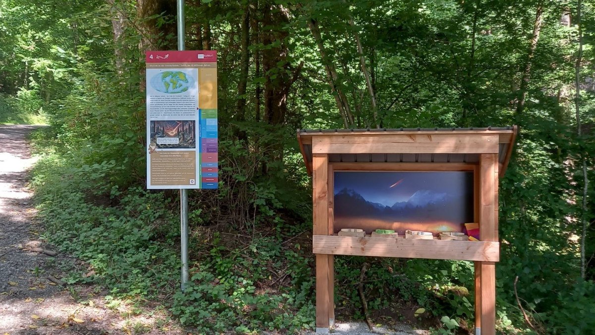 Eine Informationstafel und eine Wurfbude stehen im Wald auf dem Geopfad Gaildorf, Station 4. Die Tafel enthält geologische Informationen.