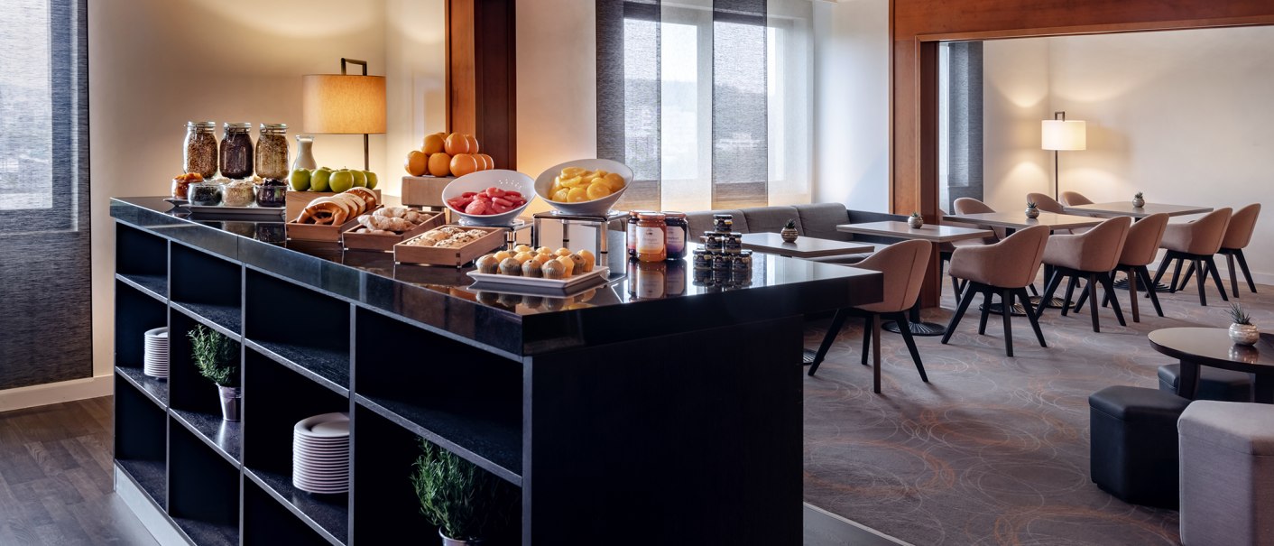 Moderne Lounge mit Frühstücksbuffet, das Obst, Gebäck und Marmeladen bietet. Im Hintergrund sind Tische und Stühle in einem eleganten Raum zu sehen., © Stuttgart Marriott Hotel Sindelfingen
