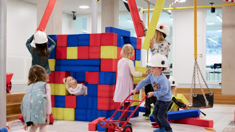 Kinder spielen auf einer Indoor-Baustelle mit bunten Schaumstoffblöcken. Sie tragen Bauhelme und haben Spaß beim Bauen und Spielen., © Julia Ochs Kinder spielen auf einer Indoor-Baustelle mit bunten Schaumstoffblöcken. Sie tragen Bauhelme und haben Spaß beim Bauen und Spielen., © Julia Ochs