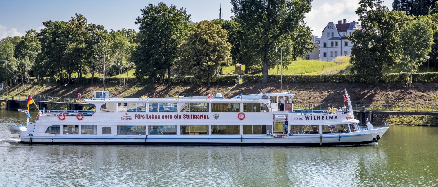 Das Passagierschiff MS Wilhelma fährt auf einem Fluss, umgeben von Bäumen und einem Gebäude im Hintergrund. Aufschrift: "Fürs Leben gern ein Stuttgarter.", © all copyrights are reserved by maks richter Das Passagierschiff MS Wilhelma fährt auf einem Fluss, umgeben von Bäumen und einem Gebäude im Hintergrund. Aufschrift: "Fürs Leben gern ein Stuttgarter.", © all copyrights are reserved by maks richter