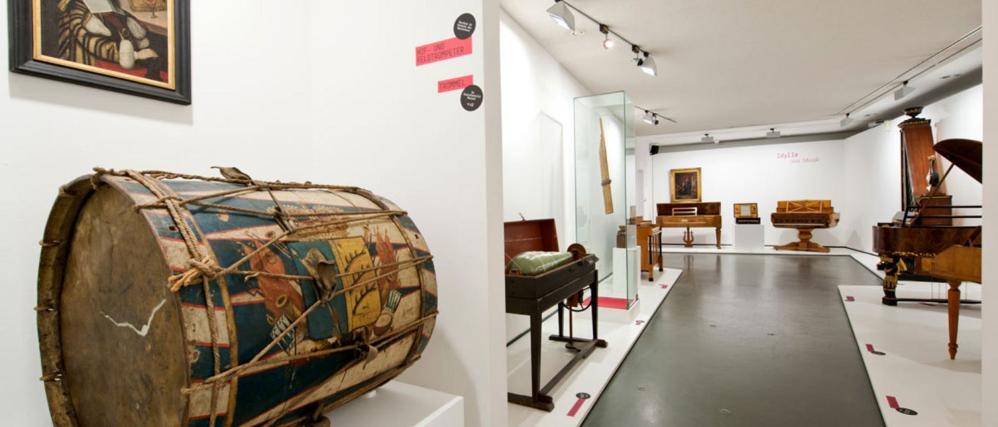 Museumsausstellung mit historischen Musikinstrumenten, darunter eine bemalte Trommel im Vordergrund und verschiedene Tasteninstrumente im Hintergrund., © Landesmuseum Württemberg