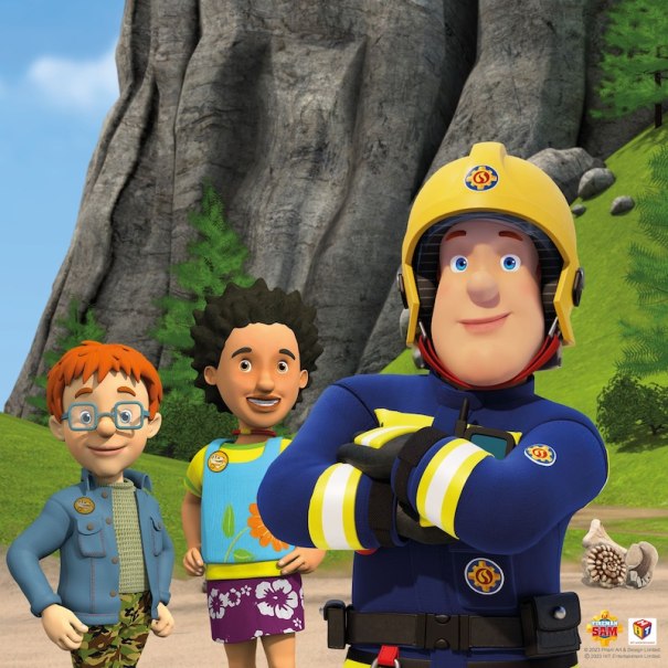 Feuerwehrmann Sam steht mit zwei Kindern vor einer Felswand. Alle lächeln und tragen bunte Kleidung. Im Hintergrund sind Bäume und Felsen zu sehen., © SBEntertainment GmbH & Co. KG