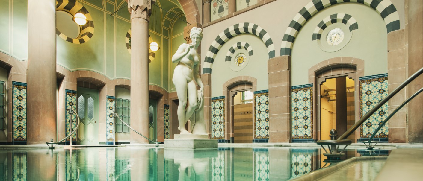 Historisches Schwimmbecken mit kunstvollen Fliesen und einer Statue in einem eleganten, gew&ouml;lbten Raum., &copy; &copy;LOCHER Fotodesign & Manufaktur &copy;Staatsbad Wildbad GmbH