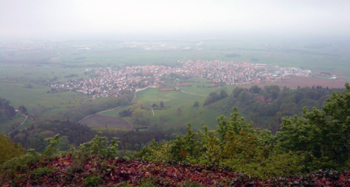 Blick von einem Hügel auf eine Stadt in der Ferne, umgeben von grünen Feldern und Bäumen. Der Himmel ist bewölkt und neblig., © Schwäbische Alb Tourismusverband e.V. Blick von einem Hügel auf eine Stadt in der Ferne, umgeben von grünen Feldern und Bäumen. Der Himmel ist bewölkt und neblig., © Schwäbische Alb Tourismusverband e.V.