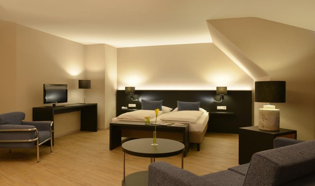 Modernes Doppelzimmer mit Doppelbett, Sofa, Fernseher und stilvoller Beleuchtung. Dezente Farben und elegantes Design schaffen eine gemütliche Atmosphäre., © relexa Waldhotel Schatten Modernes Doppelzimmer mit Doppelbett, Sofa, Fernseher und stilvoller Beleuchtung. Dezente Farben und elegantes Design schaffen eine gemütliche Atmosphäre., © relexa Waldhotel Schatten
