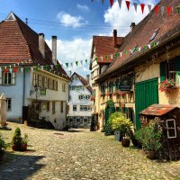 Malerische Altstadtgasse mit Kopfsteinpflaster, Fachwerkhäusern und bunten Wimpeln. Blumen schmücken die Fassaden, sonniges Wetter., © Nürtingen Malerische Altstadtgasse mit Kopfsteinpflaster, Fachwerkhäusern und bunten Wimpeln. Blumen schmücken die Fassaden, sonniges Wetter., © Nürtingen