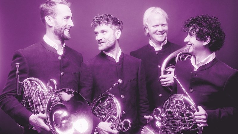 Vier M&auml;nner in dunklen Anz&uuml;gen halten H&ouml;rner und l&auml;cheln sich gegenseitig an. Das Bild ist in einem lila Farbton gehalten., &copy; Kulturstiftung Hohenlohe