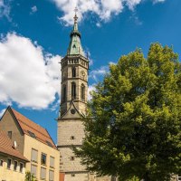 Die Amanduskirche in Bad Urach erhebt sich majestätisch neben Wohnhäusern unter einem klaren blauen Himmel mit weißen Wolken., © Stuttgart-Marketing GmbH, Sarah Schmid
