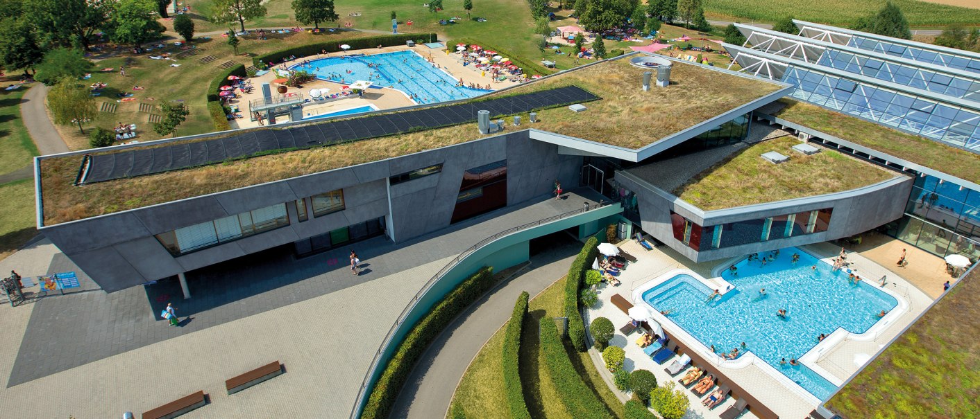 Luftaufnahme des Fildorado mit begrüntem Dach, Außenpool und Liegewiese. Menschen entspannen und schwimmen bei sonnigem Wetter., © Sport- und Badezentrum Fildorado GmbH Luftaufnahme des Fildorado mit begrüntem Dach, Außenpool und Liegewiese. Menschen entspannen und schwimmen bei sonnigem Wetter., © Sport- und Badezentrum Fildorado GmbH