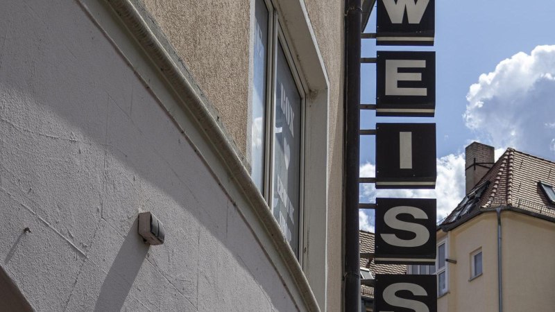 Ein Schild mit der Aufschrift 'WEISS' hängt an einem Gebäude. Der Himmel ist blau mit einigen Wolken. Im Hintergrund sind Dächer zu sehen., © SMG, Sarah Schmid Ein Schild mit der Aufschrift 'WEISS' hängt an einem Gebäude. Der Himmel ist blau mit einigen Wolken. Im Hintergrund sind Dächer zu sehen., © SMG, Sarah Schmid