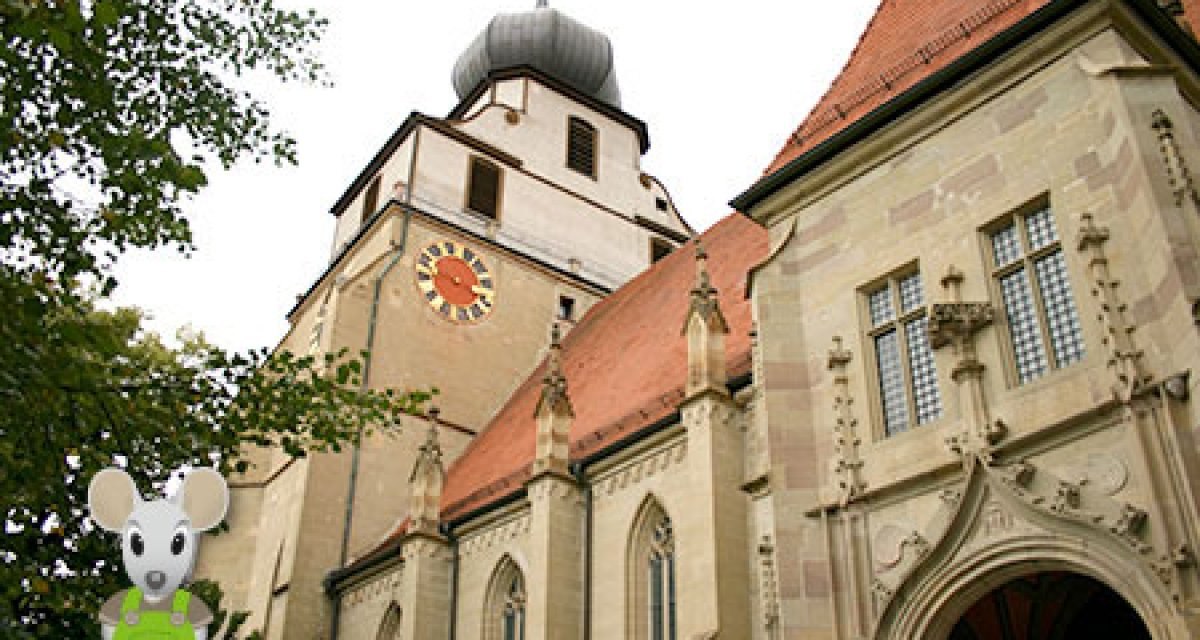 Eine Kirche mit einem markanten Uhrturm und einer Mausfigur im Vordergrund. Die Architektur ist gotisch geprägt. Eine Kirche mit einem markanten Uhrturm und einer Mausfigur im Vordergrund. Die Architektur ist gotisch geprägt.