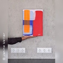 Abstrakte Leinwandmalerei mit geometrischen Formen in Rot, Blau und Orange, gehalten von einer Hand vor einer grauen Wand mit Steckdosen., &copy; links im Bild