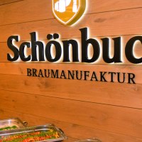 Innenansicht einer Brauerei mit Buffet. An der Holzwand steht "Schönbuch Braumanufaktur". Im Vordergrund sind Speisen in Warmhaltebehältern., © Schönbuchbrauerei, Sebastian Berger