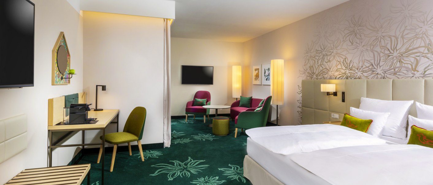 Moderne Hotelsuite mit Doppelbett, Schreibtisch, Sitzbereich und stilvoller Dekoration. Grüner Teppich und helle Wände mit floralen Mustern., © Mövenpick Hotel Stuttgart Messe & Congress Moderne Hotelsuite mit Doppelbett, Schreibtisch, Sitzbereich und stilvoller Dekoration. Grüner Teppich und helle Wände mit floralen Mustern., © Mövenpick Hotel Stuttgart Messe & Congress