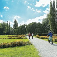 Grüne Wiese im Sommerhofenpark Sindelfingen mit Spaziergängern, Radfahrern und Blumenbeeten unter blauem Himmel., © Werberlinge