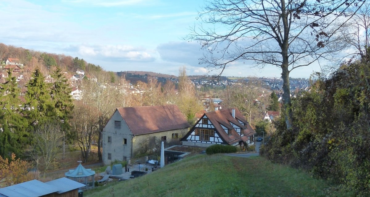 Ein schmaler Weg führt über eine grüne Wiese zu einem Fachwerkhaus. Im Hintergrund sind weitere Gebäude und eine hügelige Landschaft zu sehen., © Natur.Nah. Schönbuch & Heckengäu Ein schmaler Weg führt über eine grüne Wiese zu einem Fachwerkhaus. Im Hintergrund sind weitere Gebäude und eine hügelige Landschaft zu sehen., © Natur.Nah. Schönbuch & Heckengäu