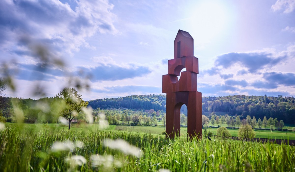 Rostfarbene Skulptur von Werner Pokorny in einer grünen Landschaft, umgeben von Wiesen und Bäumen, unter einem blauen Himmel mit Wolken., © Natur.Nah. Schönbuch & Heckengäu Rostfarbene Skulptur von Werner Pokorny in einer grünen Landschaft, umgeben von Wiesen und Bäumen, unter einem blauen Himmel mit Wolken., © Natur.Nah. Schönbuch & Heckengäu