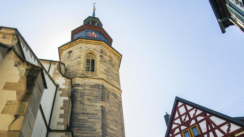 Turm einer Stadtkirche mit Uhr, daneben ein Fachwerkhaus. Der Himmel ist klar und blau., © Stuttgart-Marketing GmbH, Sarah Schmid Turm einer Stadtkirche mit Uhr, daneben ein Fachwerkhaus. Der Himmel ist klar und blau., © Stuttgart-Marketing GmbH, Sarah Schmid