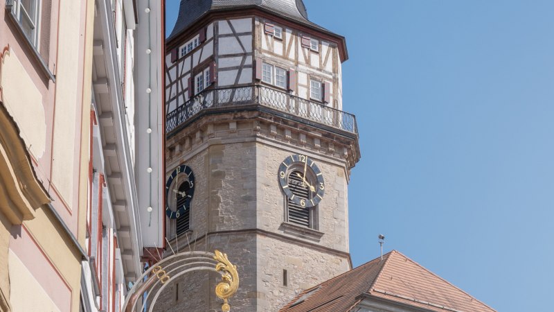 Der Backnanger Stadtturm mit Fachwerk und Uhr ragt zwischen Geb&auml;uden hervor, unter klarem, blauem Himmel., &copy; Stuttgart-Marketing GmbH, Martina Denker