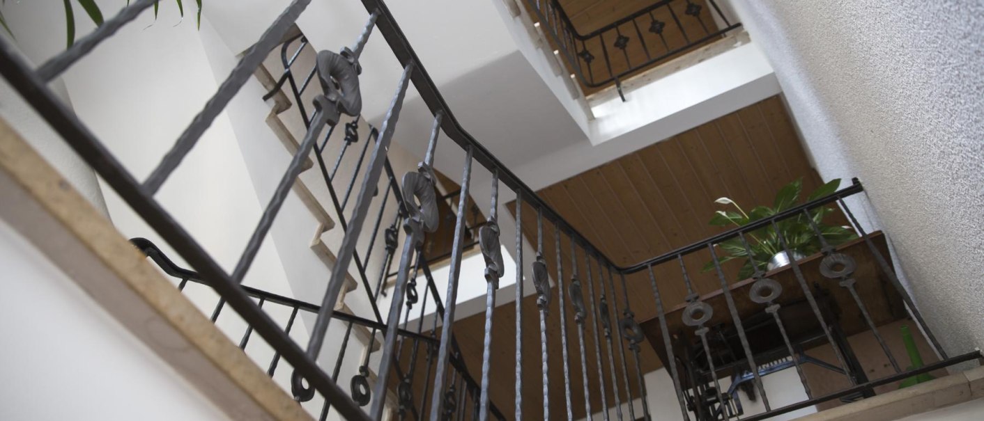 Blick nach oben in einem Treppenhaus mit schmiedeeisernem Geländer, Holzelementen und Pflanzen., © Gasthof zum Bären