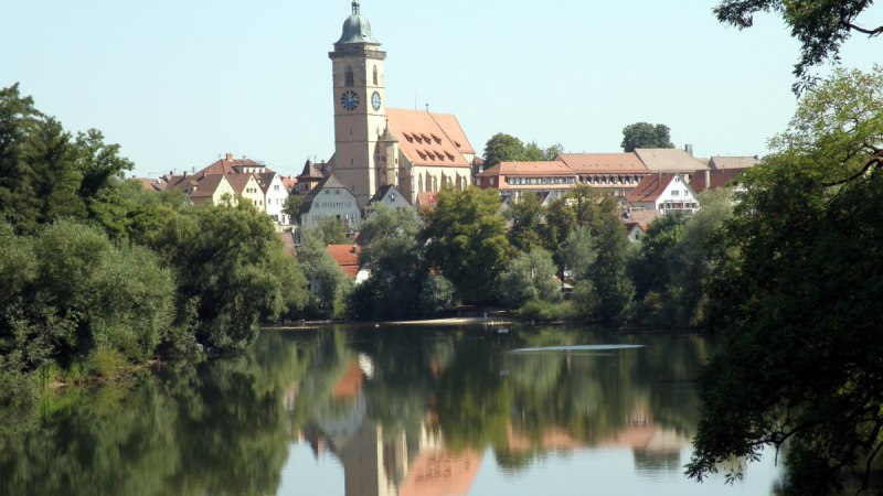 Nürtingen am Neckar mit einer Kirche im Zentrum, umgeben von Bäumen. Die Spiegelung der Stadt ist im ruhigen Wasser sichtbar., © Stadt Nürtingen Nürtingen am Neckar mit einer Kirche im Zentrum, umgeben von Bäumen. Die Spiegelung der Stadt ist im ruhigen Wasser sichtbar., © Stadt Nürtingen