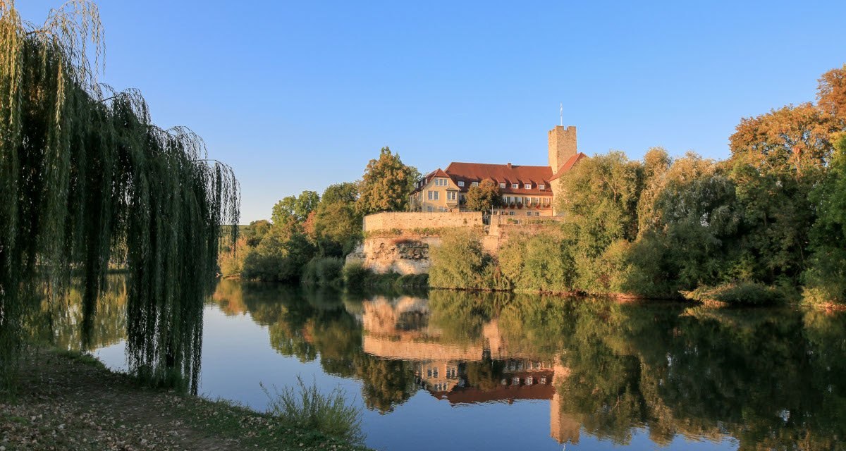 Die Rathausburg Lauffen am Neckar spiegelt sich im ruhigen Fluss. Umgeben von B&auml;umen und blauem Himmel, wirkt die Szene idyllisch und friedlich., &copy; Ulrich Seidel