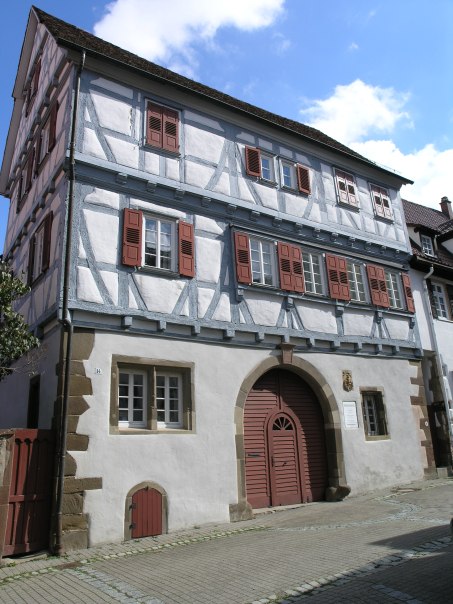 Ein traditionelles Fachwerkhaus mit roten Fensterl&auml;den und einem gro&szlig;en Holztor. Der Himmel ist blau mit einigen Wolken., &copy; Stadtmarketing Leonberg