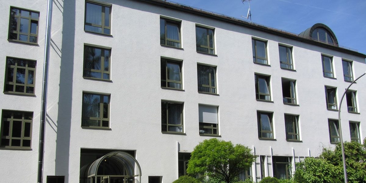 Mehrstöckiges Gebäude mit weißen Wänden und zahlreichen Fenstern, umgeben von Bäumen und Sträuchern., © Christkönigshaus Mehrstöckiges Gebäude mit weißen Wänden und zahlreichen Fenstern, umgeben von Bäumen und Sträuchern., © Christkönigshaus