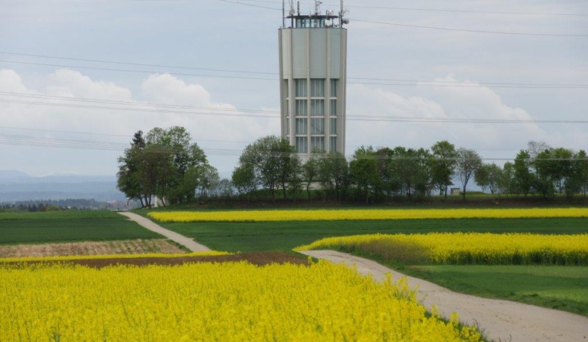 Ein Turm ragt über gelbe Rapsfelder und grüne Wiesen, umgeben von Bäumen, unter einem bewölkten Himmel., © Natur.Nah. Schönbuch & Heckengäu Ein Turm ragt über gelbe Rapsfelder und grüne Wiesen, umgeben von Bäumen, unter einem bewölkten Himmel., © Natur.Nah. Schönbuch & Heckengäu