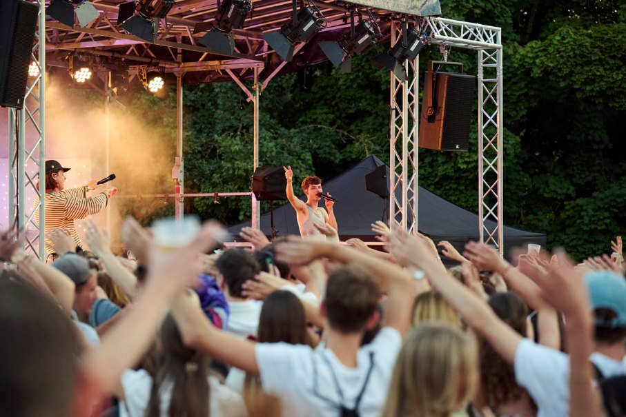 Ein S&auml;nger performt auf einer Open-Air-B&uuml;hne vor einem jubelnden Publikum. Die Zuschauer heben die H&auml;nde in die Luft, w&auml;hrend der K&uuml;nstler singt., &copy; www.peter-oppenlaender.de