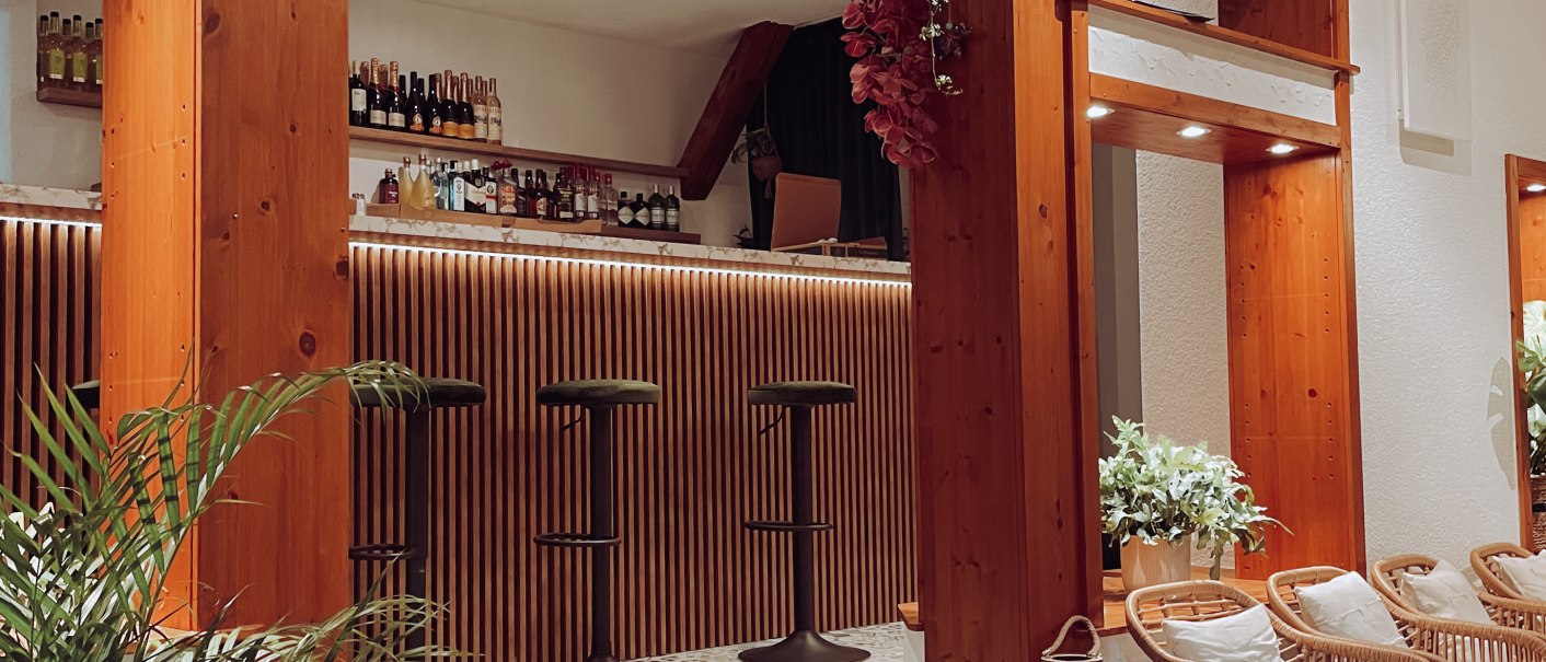 Stilvolle Bar mit Holzelementen, gemusterten Fliesen, Pflanzen und gemütlichen Sitzgelegenheiten. Einladende Atmosphäre mit moderner Einrichtung., © Jiggis
