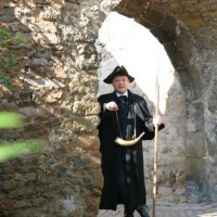 Ein Mann in historischer Kleidung mit Horn und Stab steht unter einem steinernen Torbogen und zeigt auf etwas., © WTM GmbH Waiblingen