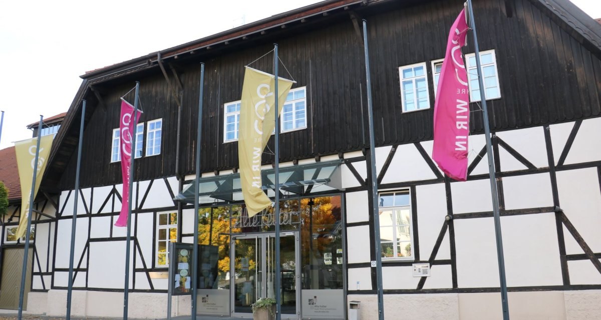 Fachwerkgeb&auml;ude mit Glasfront, beschriftet mit 'Alte Kelter'. Bunte Fahnen wehen davor. Herbstlaub liegt auf dem Boden., &copy; Remstal Tourismus e.V.