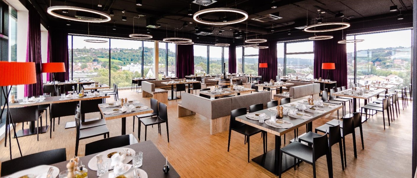 Modernes Restaurant im 7. Stock mit großen Fenstern, stilvoller Einrichtung und Blick auf eine grüne Landschaft. Runde Deckenleuchten und rote Lampen., © Hotel am Remspark Modernes Restaurant im 7. Stock mit großen Fenstern, stilvoller Einrichtung und Blick auf eine grüne Landschaft. Runde Deckenleuchten und rote Lampen., © Hotel am Remspark