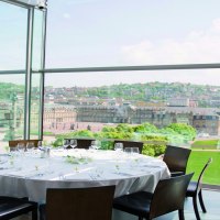 Ein runder Tisch mit weißer Tischdecke und Gläsern steht in einem verglasten Raum mit Blick auf eine Stadt und historische Gebäude., © Stuttgart-Marketing GmbH