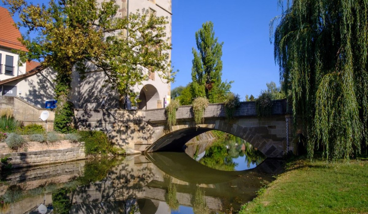 Der Beinsteiner Torturm steht neben einer Brücke, die sich im ruhigen Wasser spiegelt. Der Himmel ist klar und blau, umgeben von Bäumen., © WTM GmbH Waiblingen Der Beinsteiner Torturm steht neben einer Brücke, die sich im ruhigen Wasser spiegelt. Der Himmel ist klar und blau, umgeben von Bäumen., © WTM GmbH Waiblingen