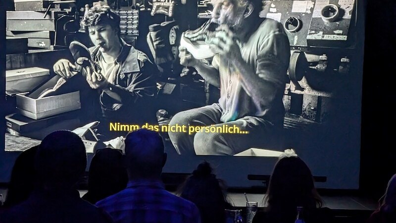 Menschen sitzen in einem Kino und schauen einen schwarz-weißen Film mit dem Untertitel: "Nimm das nicht persönlich..."., © Kulturhaus Schwanen