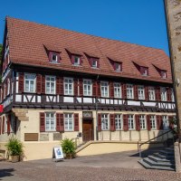Fachwerkhaus mit rotem Dach und Tourist-Info-Schild. Vor dem Gebäude sitzt eine Person auf einer Bank. Blauer Himmel im Hintergrund., © Kirchheim unter Teck
