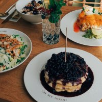 Ein Tisch mit Salat, Pfannkuchen mit Beeren, einem Getr&auml;nk und weiteren Speisen auf Holztisch., &copy; The Gardeners Nosh, Stuttgart