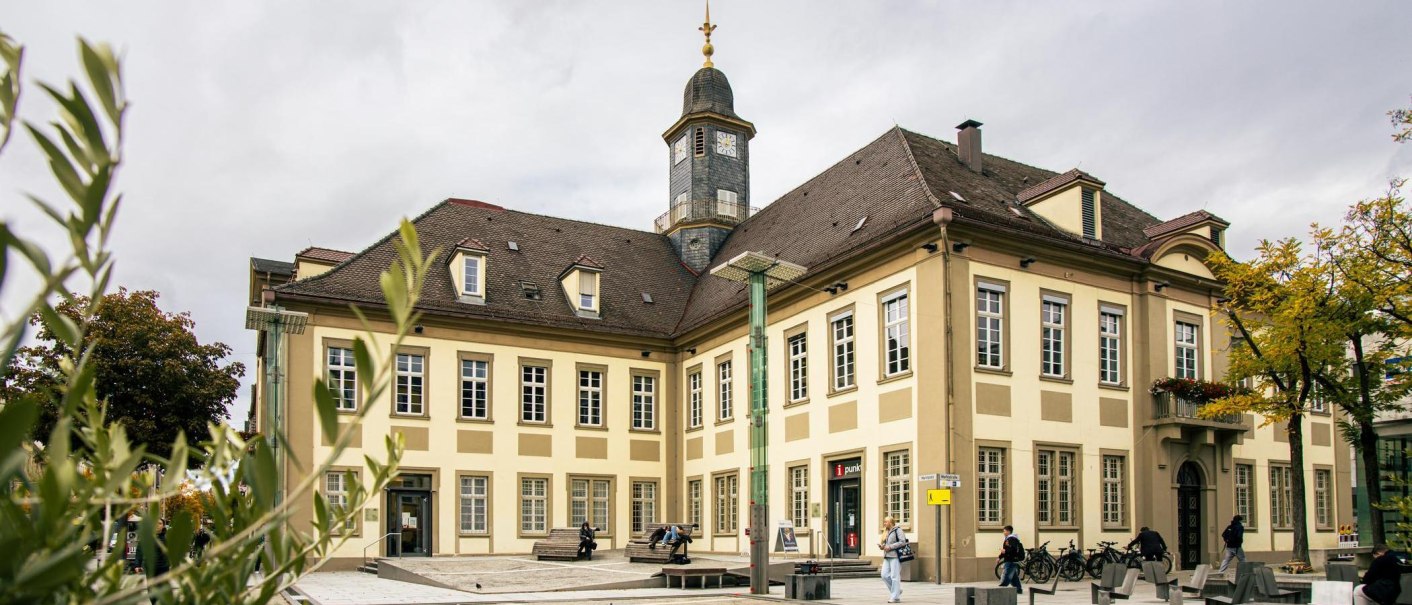 Das historische Rathaus von Göppingen am Marktplatz, umgeben von Bäumen und Menschen. Der Uhrturm ragt über das Gebäude hinaus., © SMG, Sarah Schmid Das historische Rathaus von Göppingen am Marktplatz, umgeben von Bäumen und Menschen. Der Uhrturm ragt über das Gebäude hinaus., © SMG, Sarah Schmid