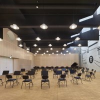 Moderner Saal mit Stühlen und Notenständern, helle Holzverkleidung, geometrische Wandmuster, hängende Lampen., © TOMAS Moderner Saal mit Stühlen und Notenständern, helle Holzverkleidung, geometrische Wandmuster, hängende Lampen., © TOMAS