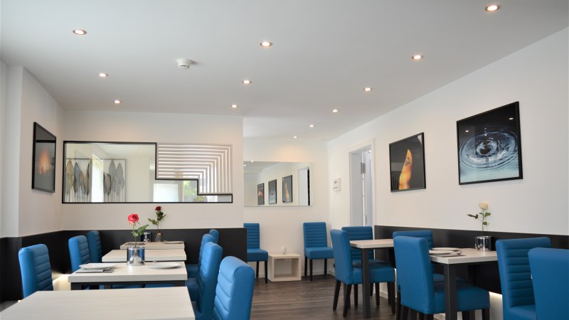 Moderner Fr&uuml;hst&uuml;cksraum mit blauen St&uuml;hlen, wei&szlig;en Tischen und dekorativen Bildern an den W&auml;nden. Dezente Beleuchtung und stilvolle Dekoration., &copy; Hotel BaW&uuml;