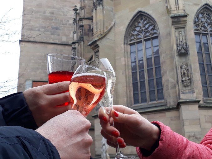 Drei Personen sto&szlig;en mit Sektgl&auml;sern vor einer historischen Kirche an. Die Gl&auml;ser enthalten rote und rosafarbene Getr&auml;nke., &copy; Eigenbetrieb Tourismus und Citymanagement Schorndorf