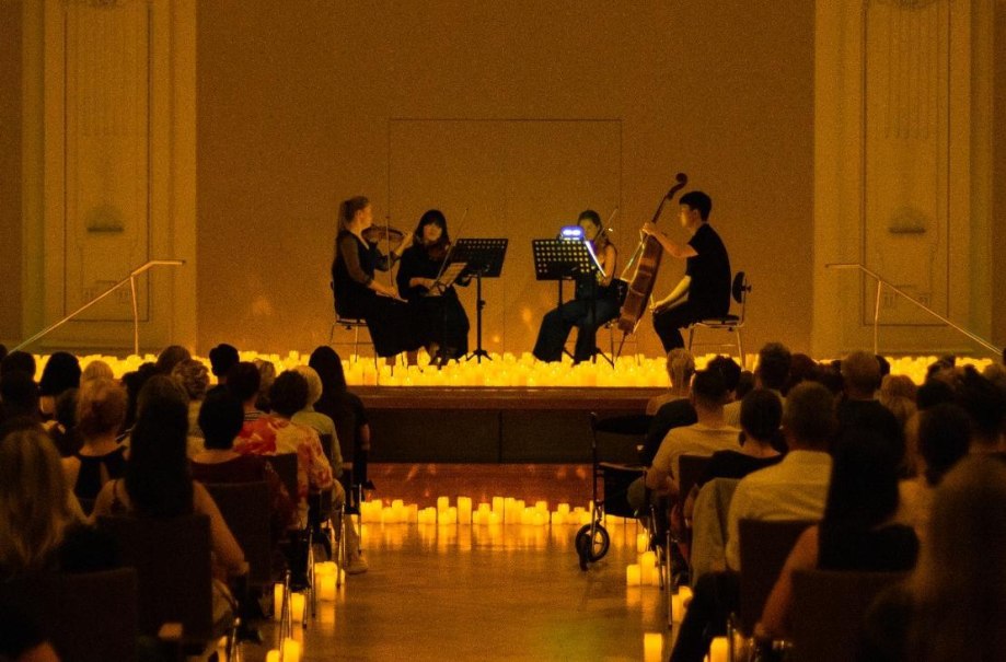 Ein Streichquartett spielt auf einer kerzenbeleuchteten B&uuml;hne vor einem sitzenden Publikum in einem Konzertsaal., &copy; FEVER
