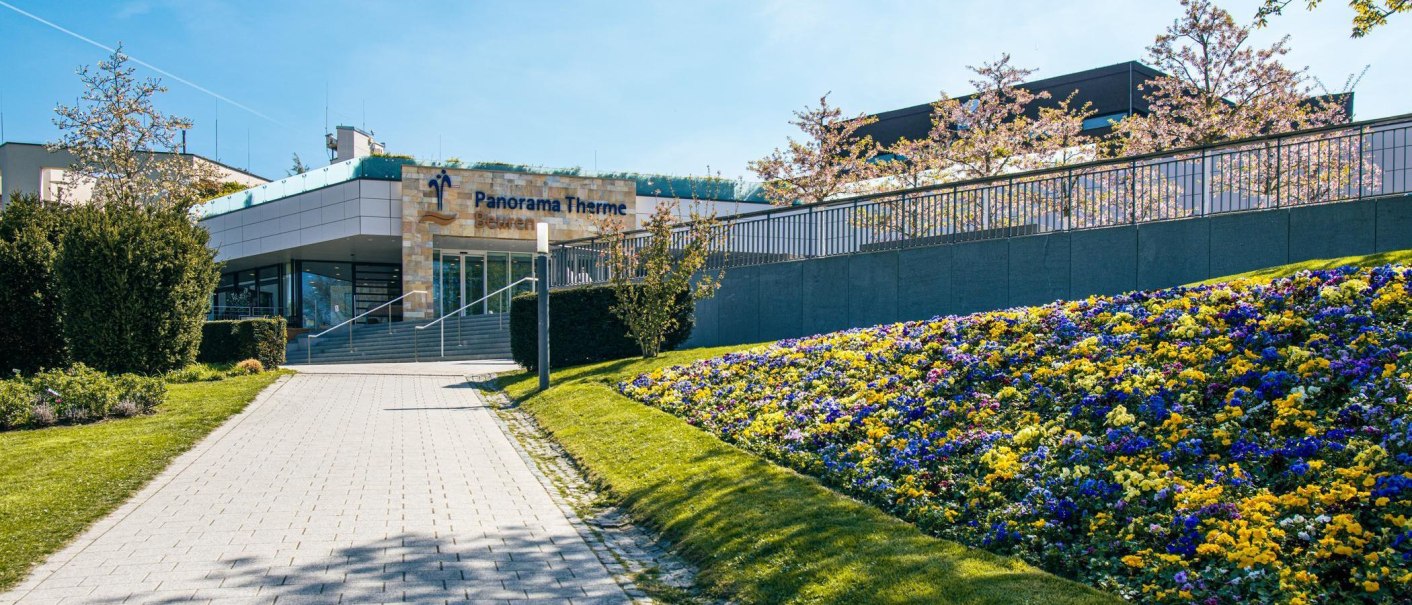 Eingang der Panorama Therme Beuren mit einem gepflegten Blumenbeet und blühenden Bäumen. Der Himmel ist klar und sonnig., © Stuttgart-Marketing GmbH, Sarah Schmid Eingang der Panorama Therme Beuren mit einem gepflegten Blumenbeet und blühenden Bäumen. Der Himmel ist klar und sonnig., © Stuttgart-Marketing GmbH, Sarah Schmid