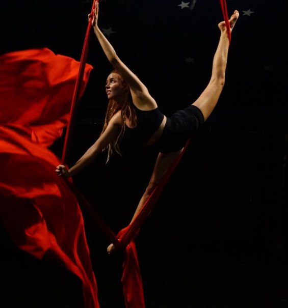 Frau in schwarzer Sportkleidung macht Luftakrobatik mit roten Tüchern in einem dunklen Raum., © Kunstschule Labyrinth